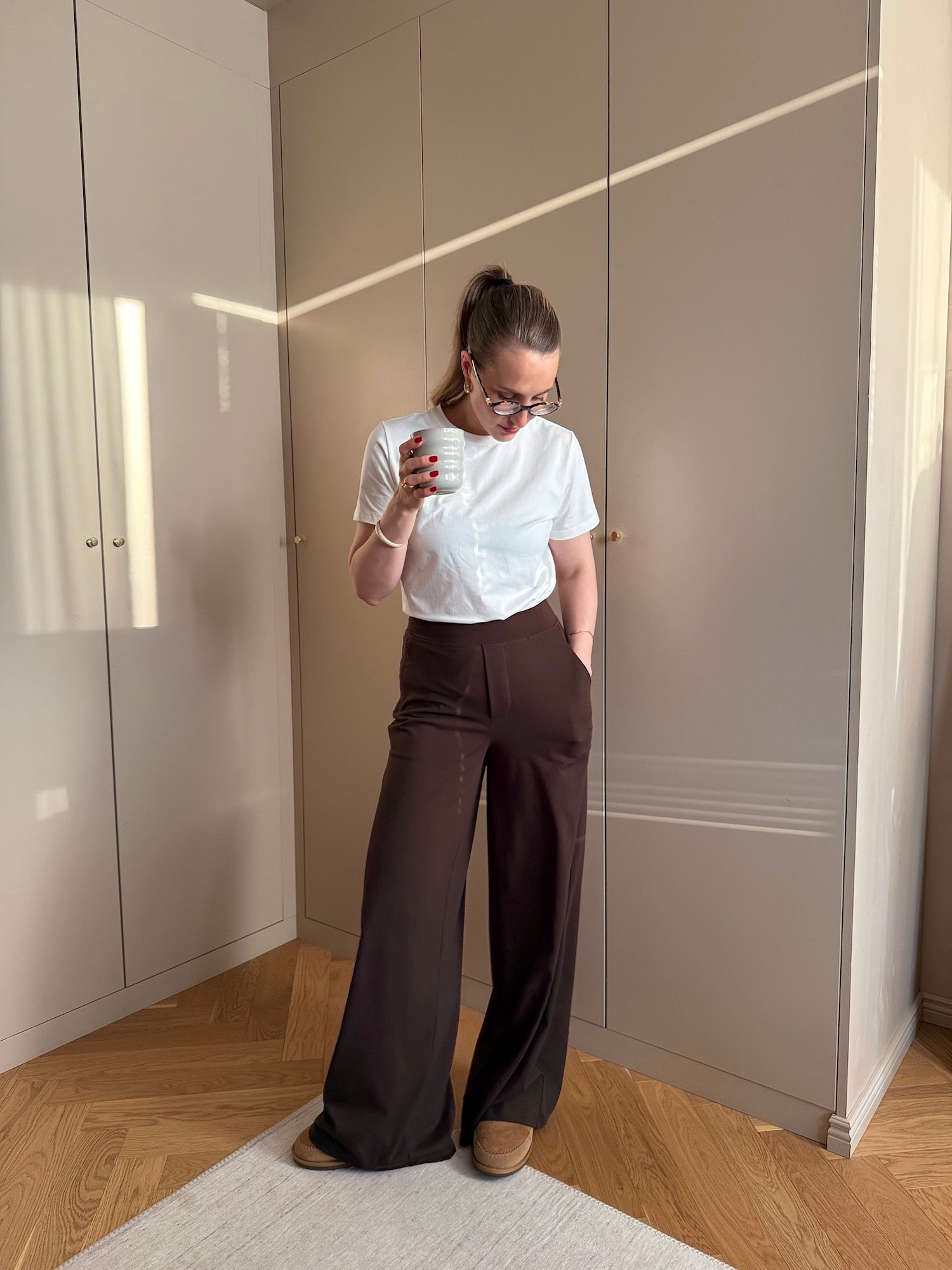 Woman wearing Ninepine Asana pants in dark brown with white Pima t-shirt, styled for a relaxed business casual outfit indoors.