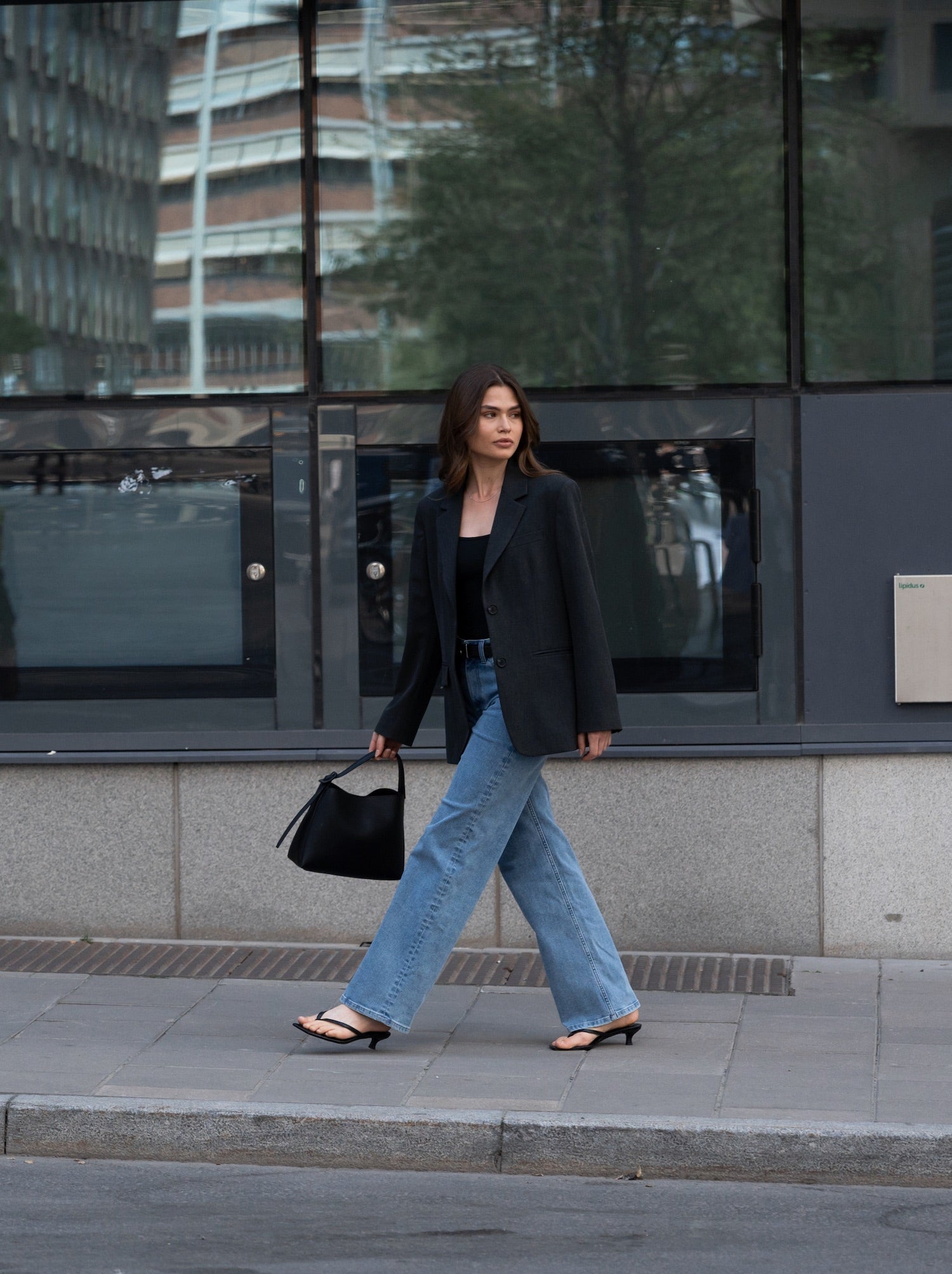 Woman wearing Ninepine relaxed ComfortDenim jeans in light blue with black Perfect Blazer, styled with bodysuit, leather belt and heels in a modern business casual street style look.